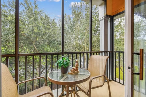 Enjoy serene views of lush greenery from the screened balcony while seated at the glass-top table. The warm-toned chairs enhance the natural light, making it a perfect spot for morning coffee or evening relaxation.