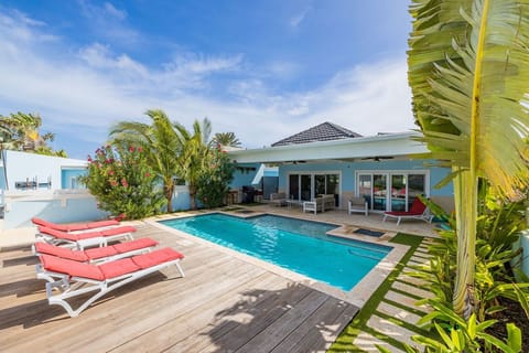 Tropical pool oasis with coral lounge chairs and lush palms framing your private retreat. Modern covered patio with BBQ and dining awaits sunny days and starlit evenings.