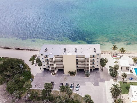 This aerial view showcases the property's prime oceanfront location, where clear turquoise water, tropical landscaping, and waterfront amenities create the perfect Florida Keys escape.