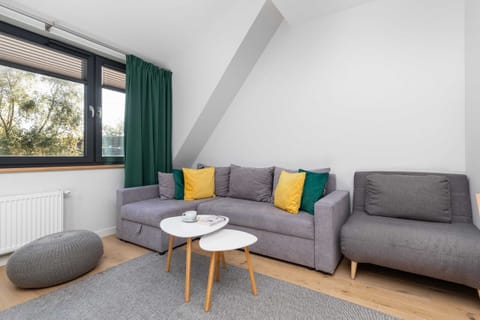 A cozy living room featuring a gray sectional sofa, green curtains, and bright natural light entering through a slanted window.