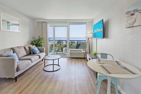 Bright, coastal-inspired living space with modern furnishings, a cozy seating area, and a private balcony showcasing stunning oceanfront views.