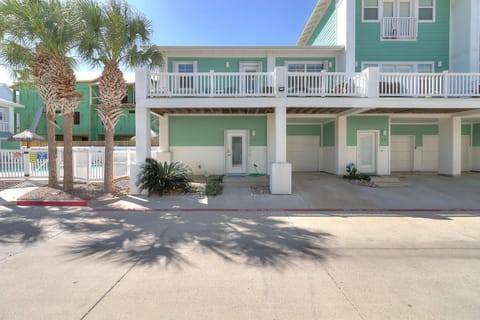 Tropical beach townhome features bright green siding, palm trees, and ground-floor parking with upstairs balconies for coastal living.