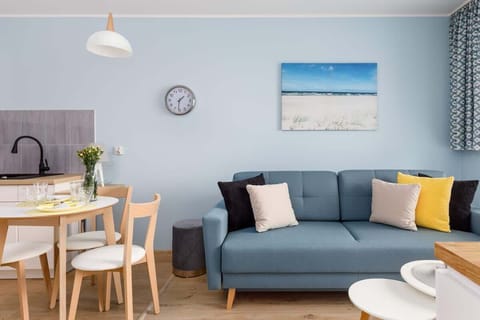 A cozy living room with a blue sofa, yellow accents, and a small dining table, creating a bright and cheerful atmosphere.
