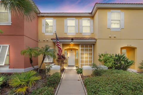 Discover a charming exterior surrounded by lush greenery and vibrant palms, inviting you to explore. The warm hues create a welcoming atmosphere, while the well-lit entryway promises cozy interiors waiting for your arrival.