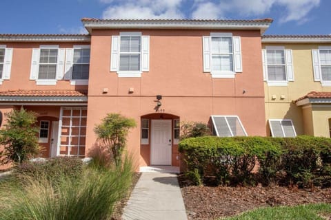Experience a vibrant escape with warm peach walls and crisp white shutters. Lush greenery welcomes you to cozy interiors, creating a bright, sunny atmosphere perfect for relaxation and exploration.