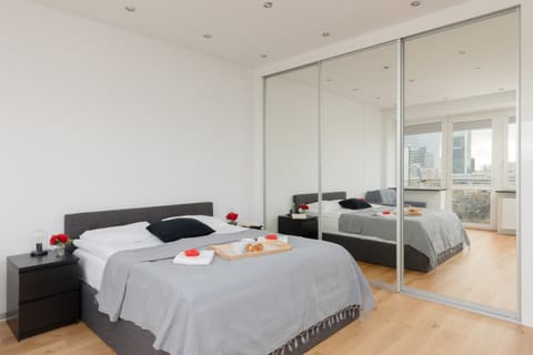 A modern bedroom with a large bed, mirrored wardrobe, and minimalistic decor for a clean, open atmosphere.
