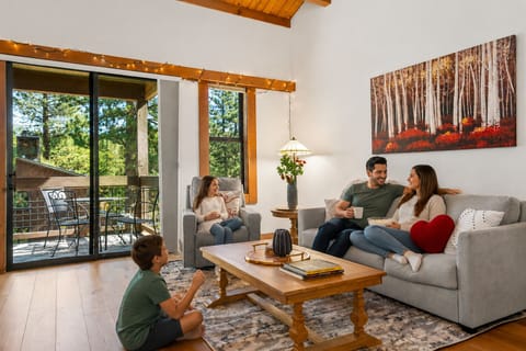 Relax in your bright, spacious living room with vaulted ceilings, cozy seating, and doors opening to a private balcony with forest views.
