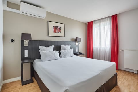 Studio sleeping area with red accent curtains and a cozy double bed, ideal for a restful city break.