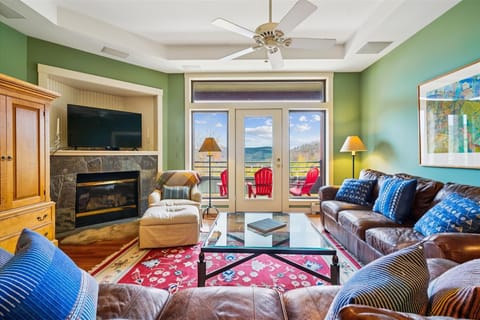 Bright living room with mountain views, leather seating, and a stone fireplace. Step out through the French doors to the deck with red Adirondack chairs and take in the Vermont scenery.