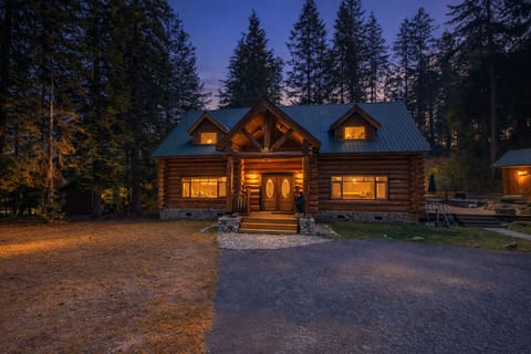 Rustic log cabin nestled among towering evergreens, glowing warmly against the twilight sky in a forest setting.