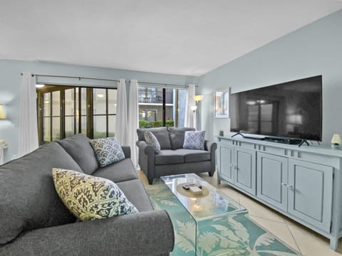 Open living room with gray sofa, blue media console, large flat screen TV, and beachy accent décor