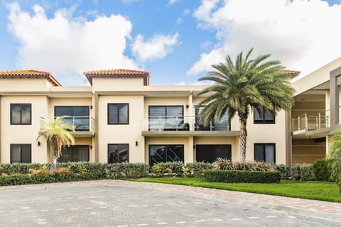 Modern two-story complex at Costa di Solo in Noord, Aruba, featuring glass balconies, tropical palm trees, and signature Mediterranean red roofs.