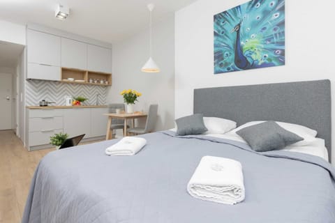The studio features a comfortable double bed with light gray bedding and a decorative pillow. A modern painting hangs above the bed, adding a stylish touch.