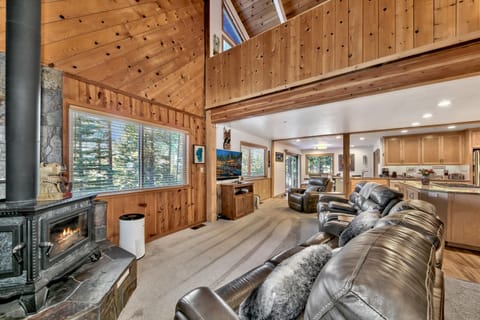 Leather recliners face a stone wood stove and large window framed by knotty pine walls in the living room.