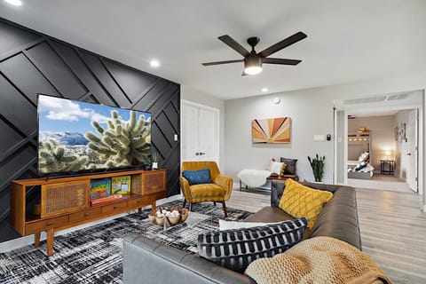 Living Room. Faux leather sofa, mustard sitting chair, clear coffee table, 65" Smart TV w/ Streaming