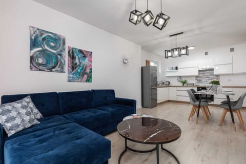 A spacious living room with a stylish blue sofa, artistic wall decor, and a coffee table, creating a cozy and modern atmosphere.
