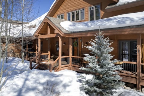 Snowy lodge entrance with a wraparound porch and rustic wood details.