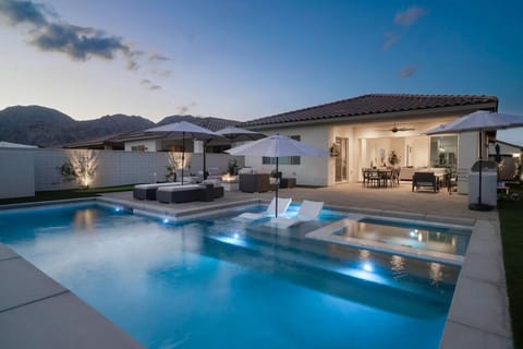 Resort-style pool glowing at dusk w/ loungers & covered patio for effortless outdoor living