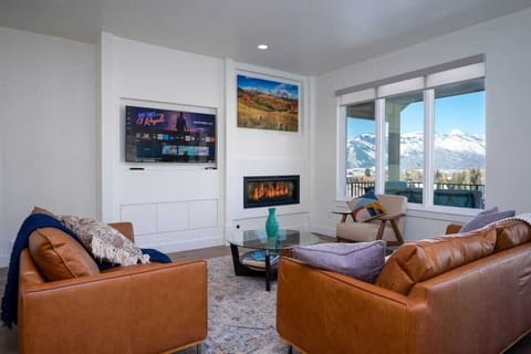 Experience the charm of Powder Ridge Escape's cozy living room, outfitted with plush seating, an expansive smart TV, and gas fireplace. Enjoy the large windows that frame the breathtaking mountain vistas.