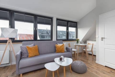 A bright and modern living room with a large gray sofa, decorative pillows in mustard yellow, and a round white coffee table. Natural light enters through large windows.