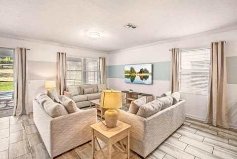 Spacious private living room with plush seating, a wall-mounted TV, and windows overlooking the landscaped outdoors.