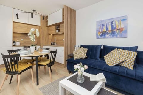 A cozy living room featuring a dark blue sofa and a small dining table with chairs. The space has a modern, minimalist vibe with light wood furniture and decor.