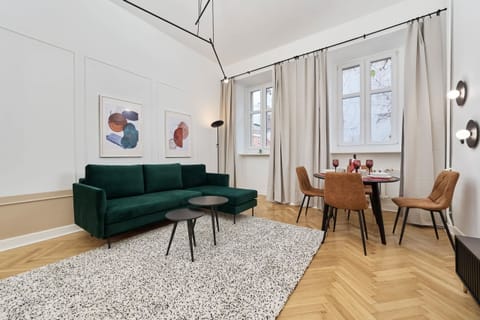 A cozy living room with a green sofa, a round coffee table, and a modern rug on wooden flooring, complemented by natural light from the windows.