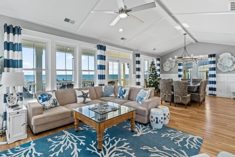 Bright living room with built-in TV storage, coastal decor, large windows, striped curtains, plush seating, and beautiful ocean views.