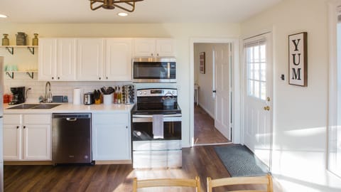 Newly renovated kitchen viewed from dining room. Electric stove, microwave, dishwasher, dual sink, toaster. Backdoor and view to third bedroom