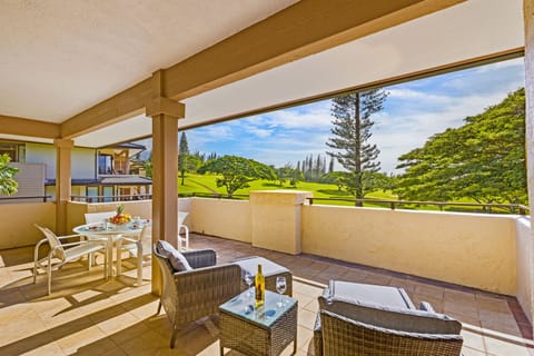 Spacious covered lanai with table seating for six and relaxing lounge chairs, surrounded by tropical foliage and resort ambiance.