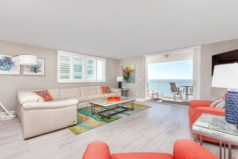 Spacious beachfront condo living room with modern decor, featuring a large sectional sofa, vibrant orange armchairs, and a stunning ocean view through the sliding glass doors