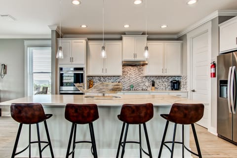 - Gather around a spacious kitchen island perfect for morning coffee or casual bites with friends
- Sleek white cabinetry, herringbone backsplash, & stainless appliances elevate the space
- Pendant lighting adds a warm glow & modern charm to every meal