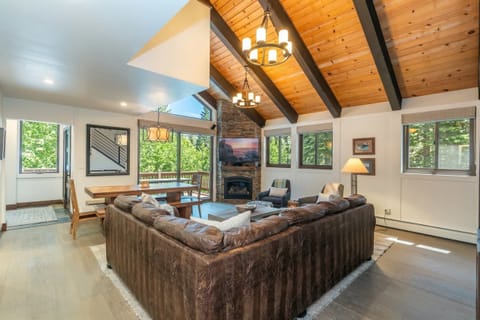 The living room features a spacious sectional sofa, two lounge chairs with ottomans, a coffee table set up around the 55” mounted flat-screen TV, and a gas fireplace in a beautiful floor-to-ceiling stone hearth.