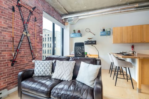 Charming vintage-style living room with a simulated brick accent wall and large windows showcasing stunning 8th-floor city views