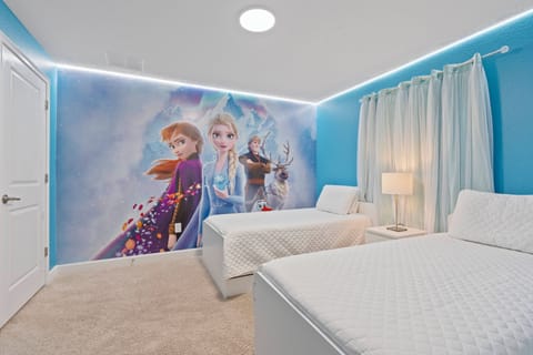 This bright bedroom features a playful blue accent wall and fun characters, creating a cheerful space for young guests. With soft carpeting, cozy bedding, and natural light filtering through sheer curtains, comfort and warmth.