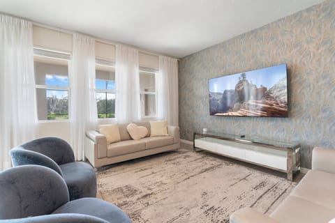 This inviting living room boasts plush, modern seating in soft tones and a sleek TV above a stylish console, with natural light streaming through elegant sheer curtains, creating a warm and relaxing atmosphere for guests.