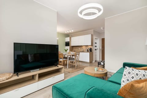 A view of the living room with a mounted TV, green accents, and a stylish chandelier.
