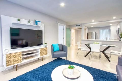 Bright living room with TV, blue rug, chairs, and dining table
