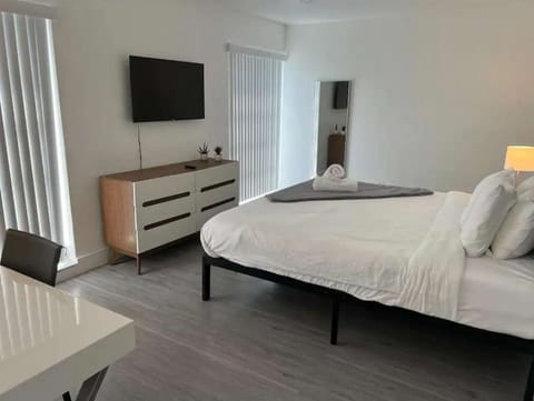 Bright bedroom with large bed, dresser, mirror, and wall TV