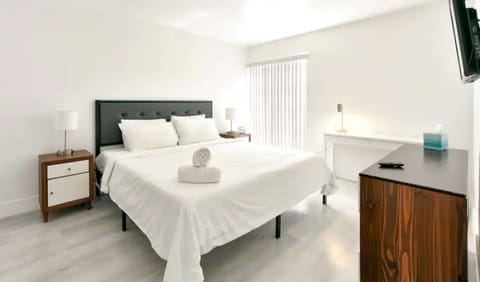 Bright king bedroom with desk, dresser, lamp, and wall TV