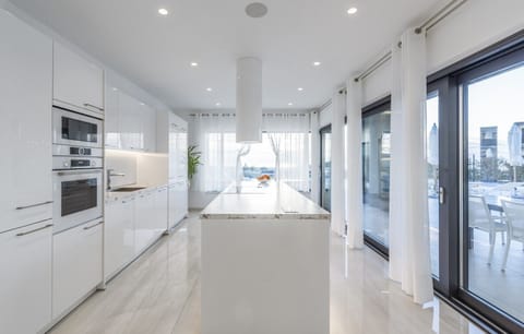 The dominance of white color in the interior of a modern kitchen with a kitchen island, stove, oven and access to a sunny terrace
