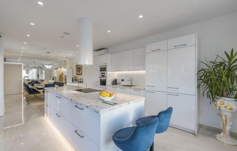 Two blue velvet bar stools behind the kitchen island and LED lighting at the base of the island and on some kitchen elements