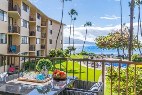 Oceanview lanai with outdoor seating overlooking lush tropical gardens, swaying palm trees, and the blue Pacific just beyond the resort grounds.