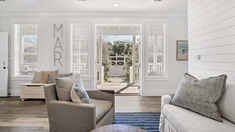 - Open concept layout with French doors that lead to a sunny porch and outdoor views - Tall windows bathe the space in natural light, highlighting clean white interiors - “MAR” wall art and simple decor bring playful, seaside charm to the space