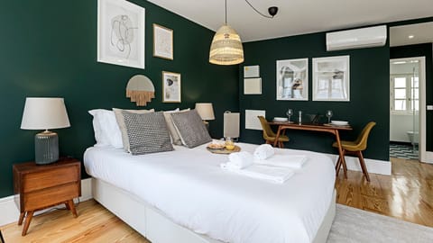 Relax in this thoughtfully designed bedroom, where rich emerald walls create a serene ambiance, complemented by a comfortable bed and a small dining setup for intimate meals or morning coffee.