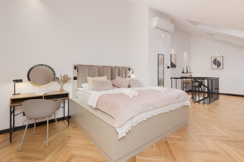 A bright bedroom featuring a double bed, soft pink bedding, and a stylish desk with a mirror.
