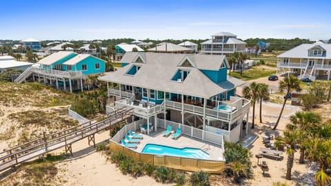 A beachfront neighborhood of coastal homes surrounded by sandy dunes and swaying palms, where this property offers a private pool and easy beach access via a raised walkway.