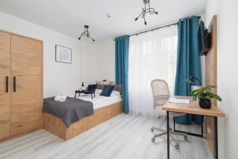 A modern bedroom with wooden furniture, gray bedding, and a workspace by the window.
