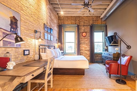 Loft Four at 124 Lofts - exposed brick walls, timber beam ceiling, king bed, writing desk, and red leather reading chair in a sun-filled historic loft.