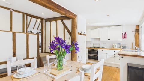 Open-plan living space at The Cote featuring sofas, Smart TV, farmhouse dining table and views into the kitchen, all in warm country style.